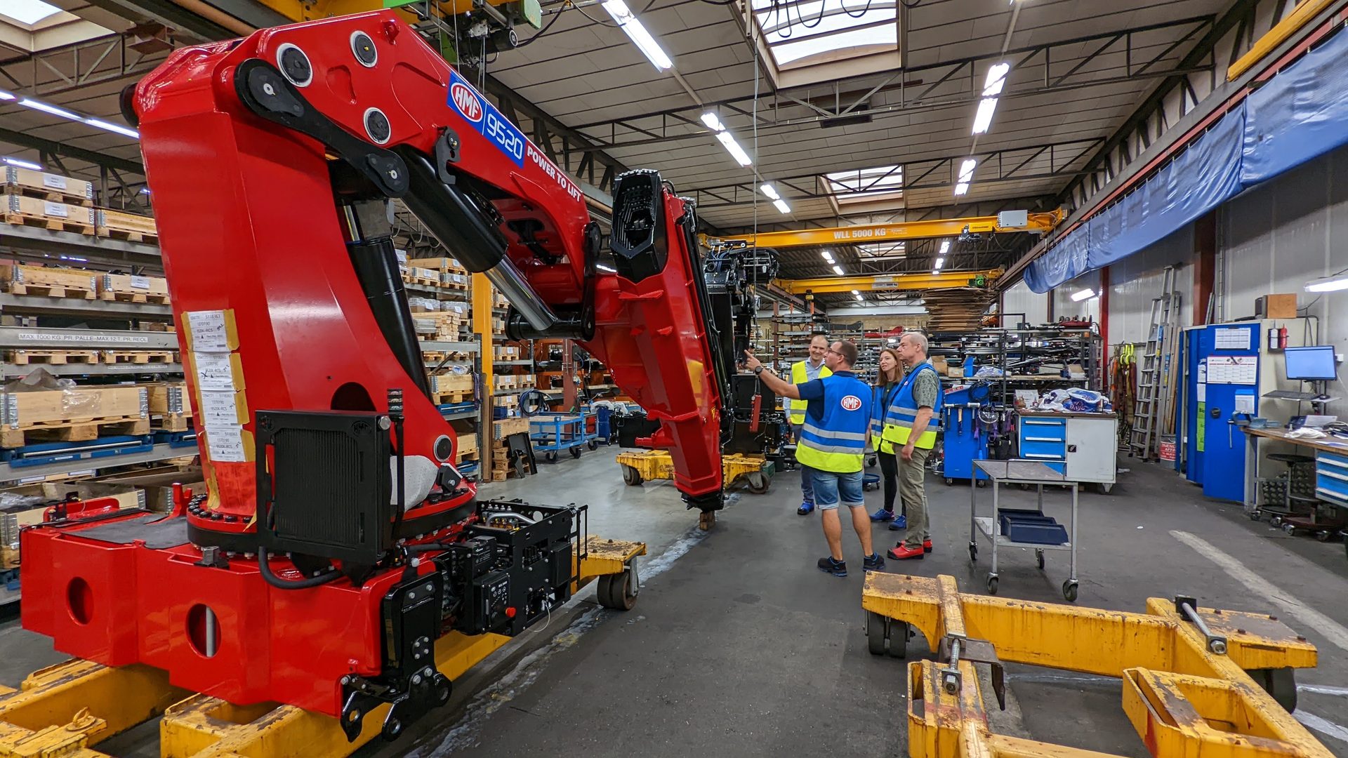 A bright red HMF loader crane on the manufacturing floor with staff around it